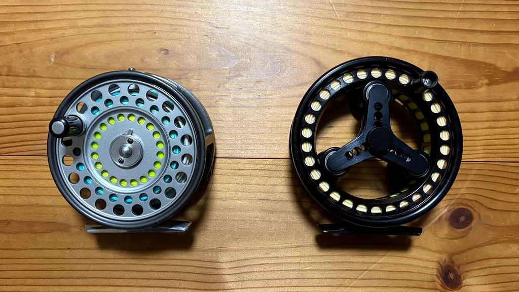 シルバーとブラックのフライリールを並べた写真。シルバーのリール（クラシックスプール）には黄緑色のバッキングラインと水色のフライラインが巻かれている。ブラックのリール（ラージアバー）はバッキングはほぼ無しで薄いオレンジ色のラインが巻かれている。
